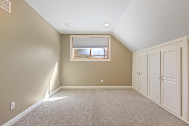 additional living space featuring light colored carpet, visible vents, lofted ceiling, and baseboards