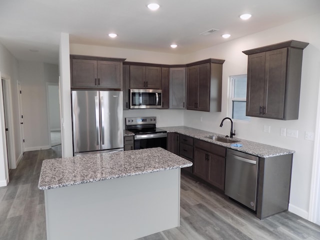 kitchen with sink, stainless steel appliances, light stone counters, and a center island