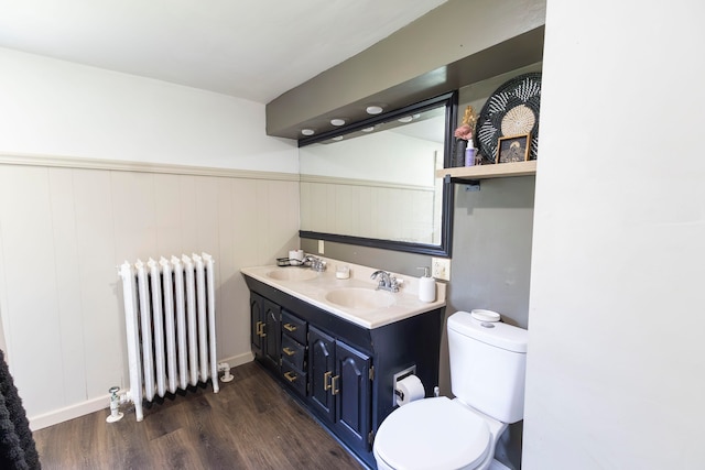 bathroom with wood-type flooring, toilet, double vanity, and radiator