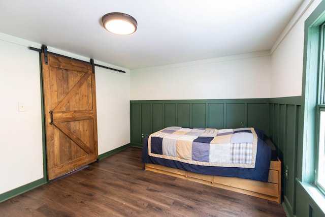 bedroom with ornamental molding, a barn door, and dark wood-type flooring