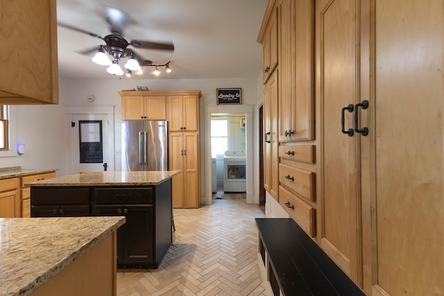 kitchen featuring high end refrigerator, light stone counters, a kitchen island, ceiling fan, and washer / dryer