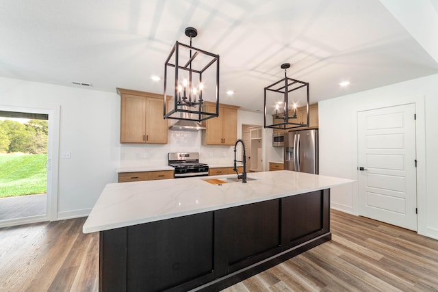 kitchen with an island with sink, hanging light fixtures, sink, appliances with stainless steel finishes, and light hardwood / wood-style floors