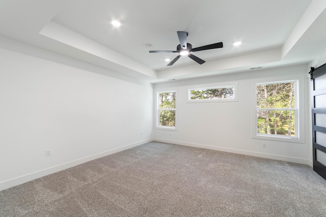 carpeted empty room featuring ceiling fan, a raised ceiling, and a barn door