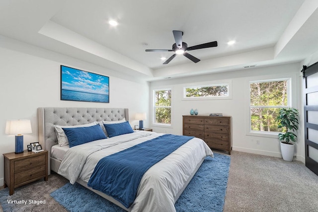 carpeted bedroom with a barn door, a raised ceiling, and ceiling fan