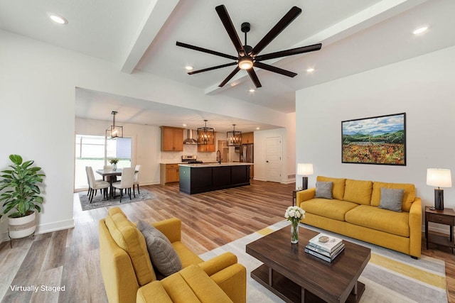 living room with light wood-type flooring, ceiling fan with notable chandelier, sink, and beamed ceiling