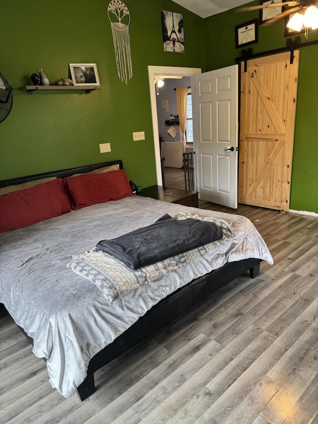 bedroom featuring ceiling fan, a barn door, and hardwood / wood-style floors