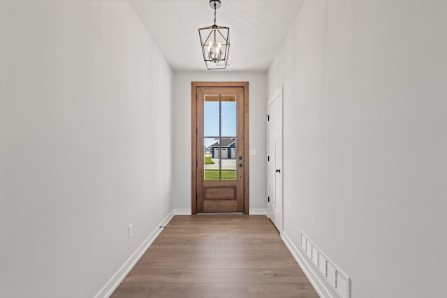 entryway featuring baseboards, visible vents, an inviting chandelier, and wood finished floors