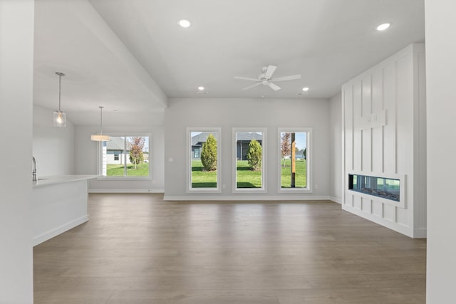 unfurnished living room with recessed lighting, a glass covered fireplace, and wood finished floors
