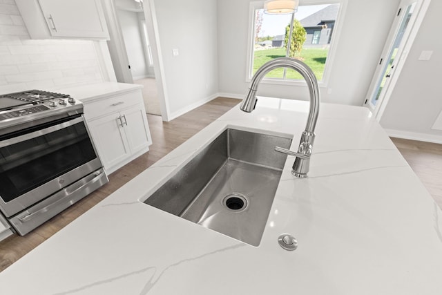 kitchen featuring dark hardwood / wood-style floors, white cabinets, decorative backsplash, stainless steel gas stove, and light stone countertops