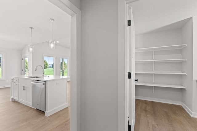 hallway featuring baseboards, a sink, vaulted ceiling, and light wood-style floors