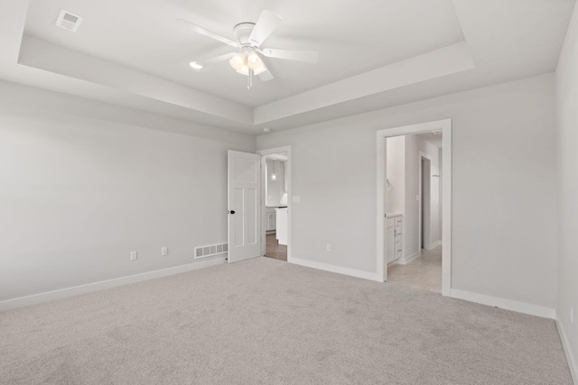 unfurnished bedroom with ceiling fan, connected bathroom, a raised ceiling, and light carpet