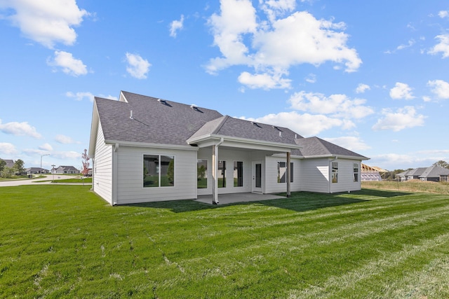 rear view of house featuring a lawn, roof with shingles, and a patio