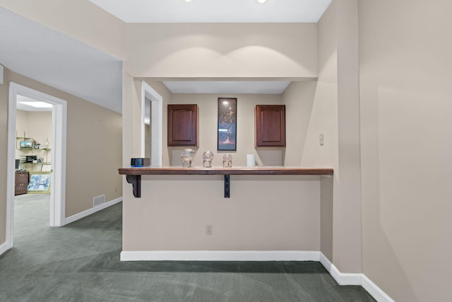 kitchen with a peninsula, visible vents, baseboards, dark colored carpet, and a kitchen bar