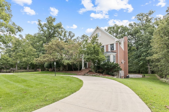 view of front of home featuring concrete driveway, a front lawn, a chimney, and brick siding