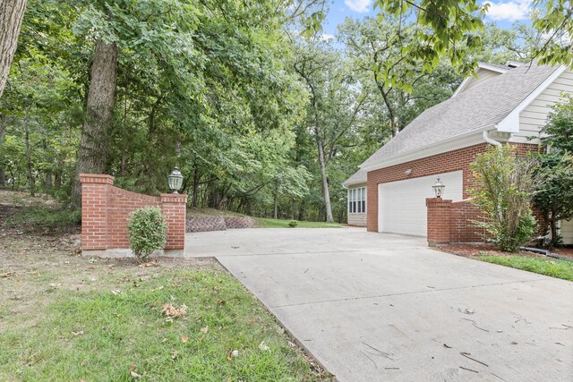 view of side of home with driveway, brick siding, and an attached garage