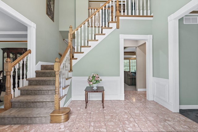 stairway featuring a decorative wall, visible vents, ornamental molding, and wainscoting