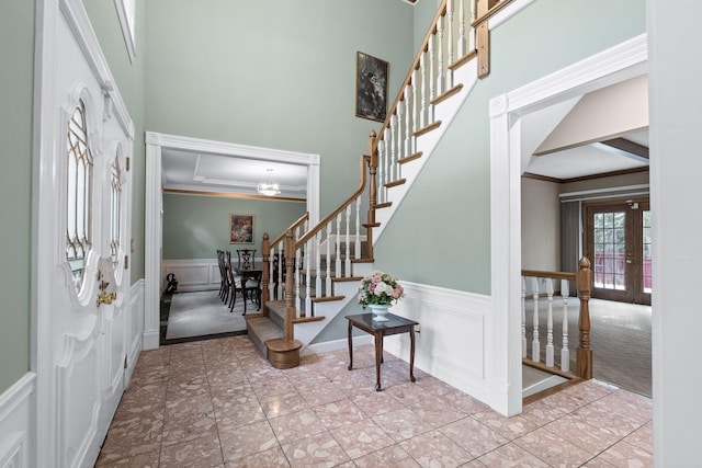 entryway with french doors, a decorative wall, ornamental molding, wainscoting, and stairs