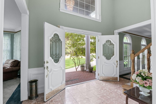 entryway featuring light tile patterned floors, a towering ceiling, ornamental molding, stairway, and wainscoting