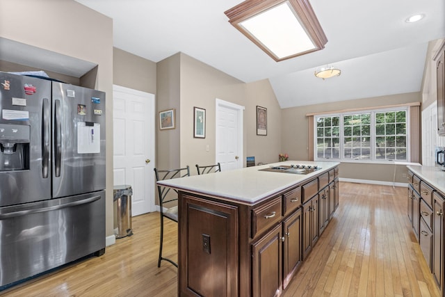 kitchen with black electric cooktop, a kitchen breakfast bar, light countertops, a center island, and stainless steel fridge