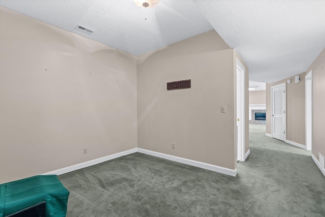 interior space featuring a textured ceiling, baseboards, a fireplace with raised hearth, and carpet flooring