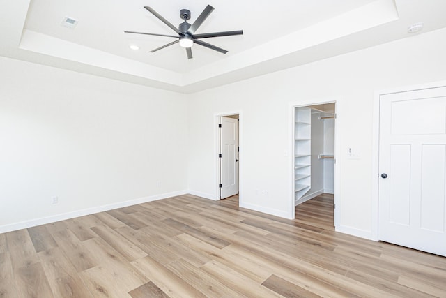 unfurnished bedroom with visible vents, baseboards, a raised ceiling, a spacious closet, and light wood-type flooring