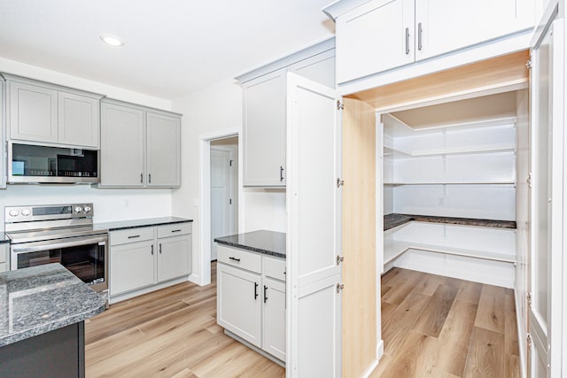 kitchen with light hardwood / wood-style floors, stainless steel appliances, dark stone countertops, and gray cabinetry