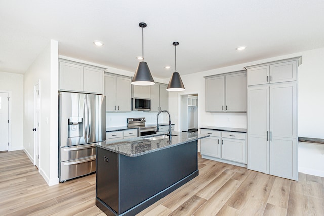 kitchen featuring appliances with stainless steel finishes, light hardwood / wood-style flooring, an island with sink, and dark stone counters