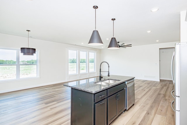 kitchen with light wood finished floors, baseboards, appliances with stainless steel finishes, light stone counters, and a sink