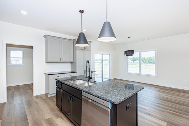 kitchen with light wood-type flooring, stainless steel dishwasher, hanging light fixtures, and a kitchen island with sink