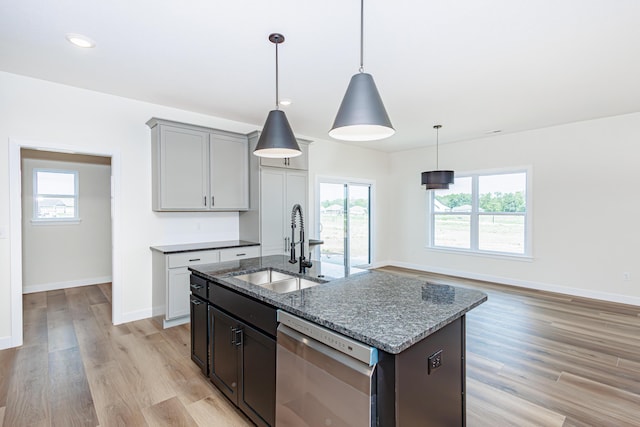 kitchen featuring stainless steel dishwasher, dark stone countertops, a sink, and light wood-style flooring