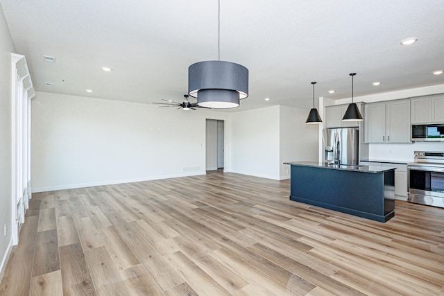 kitchen with light wood-type flooring, gray cabinetry, decorative light fixtures, a center island with sink, and stainless steel appliances