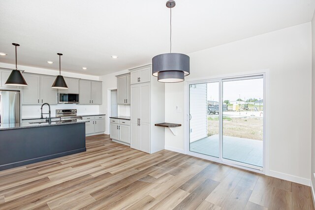 kitchen featuring stainless steel appliances, decorative light fixtures, sink, light wood-type flooring, and gray cabinetry