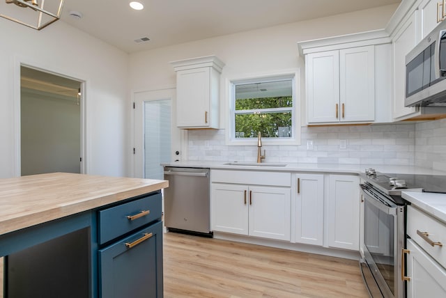 kitchen featuring tasteful backsplash, white cabinets, blue cabinets, appliances with stainless steel finishes, and light hardwood / wood-style floors