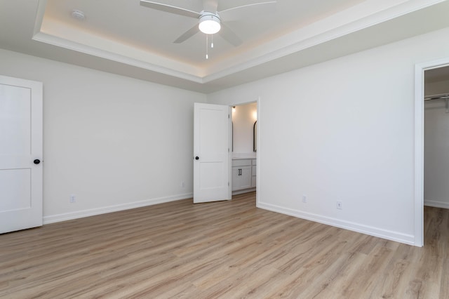 unfurnished bedroom with a tray ceiling, ceiling fan, light hardwood / wood-style floors, and a closet