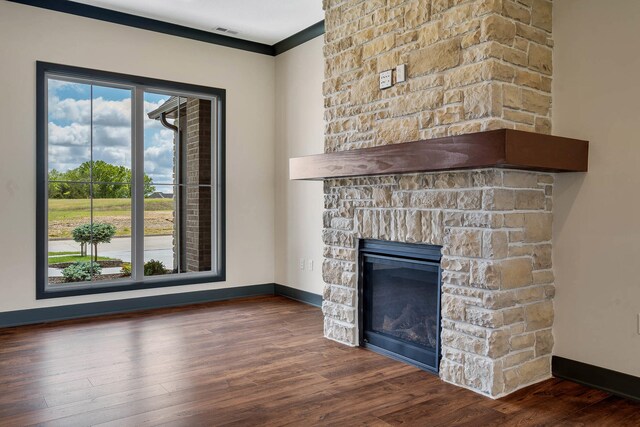 unfurnished living room with dark hardwood / wood-style floors, crown molding, and a stone fireplace