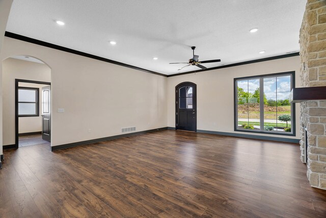 unfurnished living room featuring a textured ceiling, a stone fireplace, dark wood-type flooring, crown molding, and ceiling fan