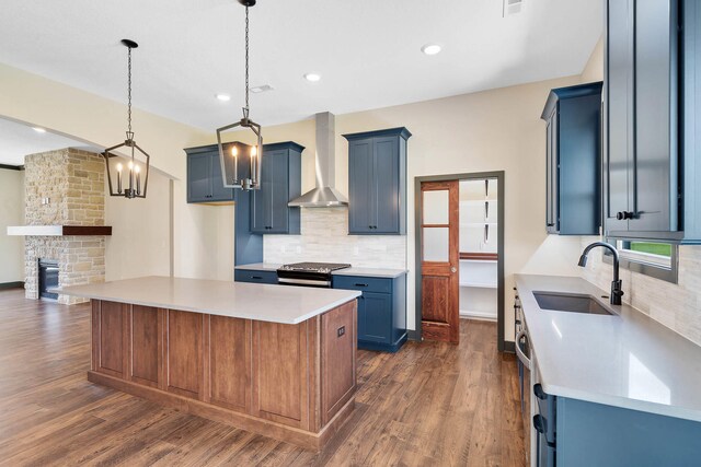 kitchen with dark hardwood / wood-style flooring, a fireplace, hanging light fixtures, sink, and wall chimney range hood