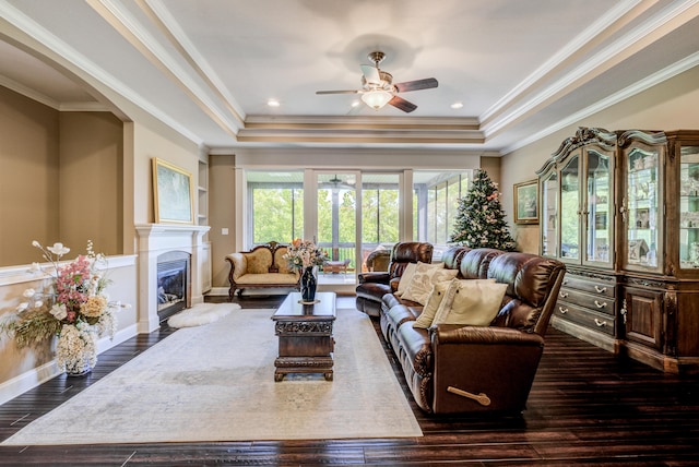 living room featuring dark wood-type flooring, ceiling fan, a raised ceiling, and ornamental molding