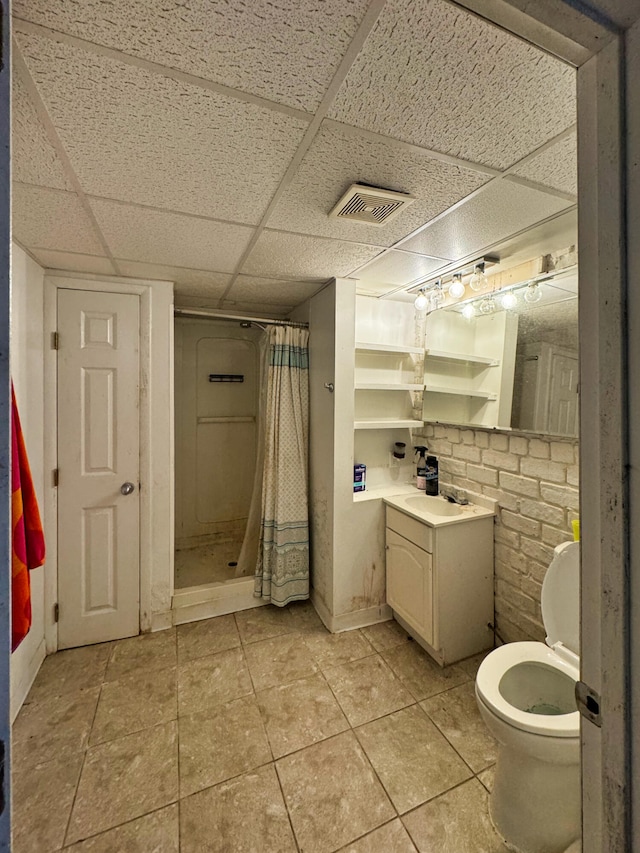 bathroom with a shower with curtain, a drop ceiling, toilet, and tile patterned floors