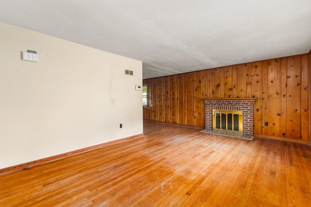 unfurnished living room featuring a brick fireplace, hardwood / wood-style flooring, and wooden walls