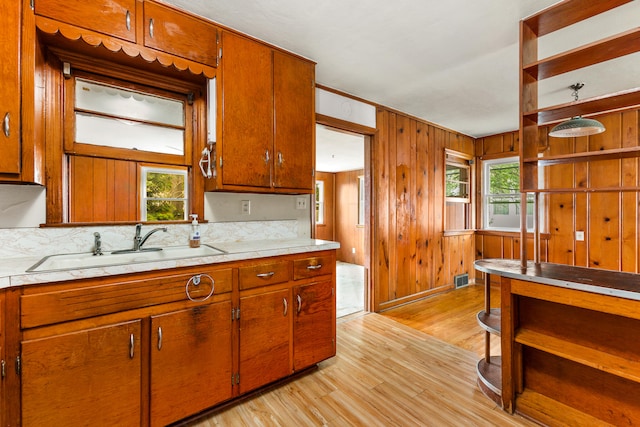 kitchen with light wood-type flooring, wooden walls, and sink