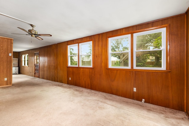 carpeted spare room featuring wood walls, ceiling fan, and a healthy amount of sunlight