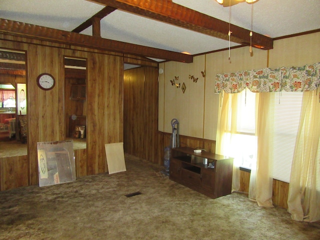 interior space with a textured ceiling, beamed ceiling, wood walls, and carpet