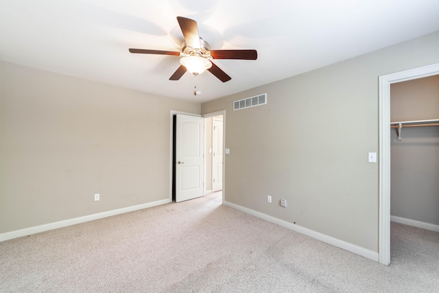 unfurnished bedroom with a walk in closet, ceiling fan, light colored carpet, and a closet