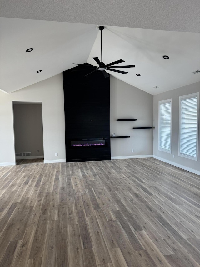 unfurnished living room featuring ceiling fan, lofted ceiling, a fireplace, and light wood-type flooring