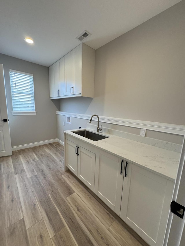 clothes washing area featuring washer hookup, sink, light hardwood / wood-style flooring, and cabinets