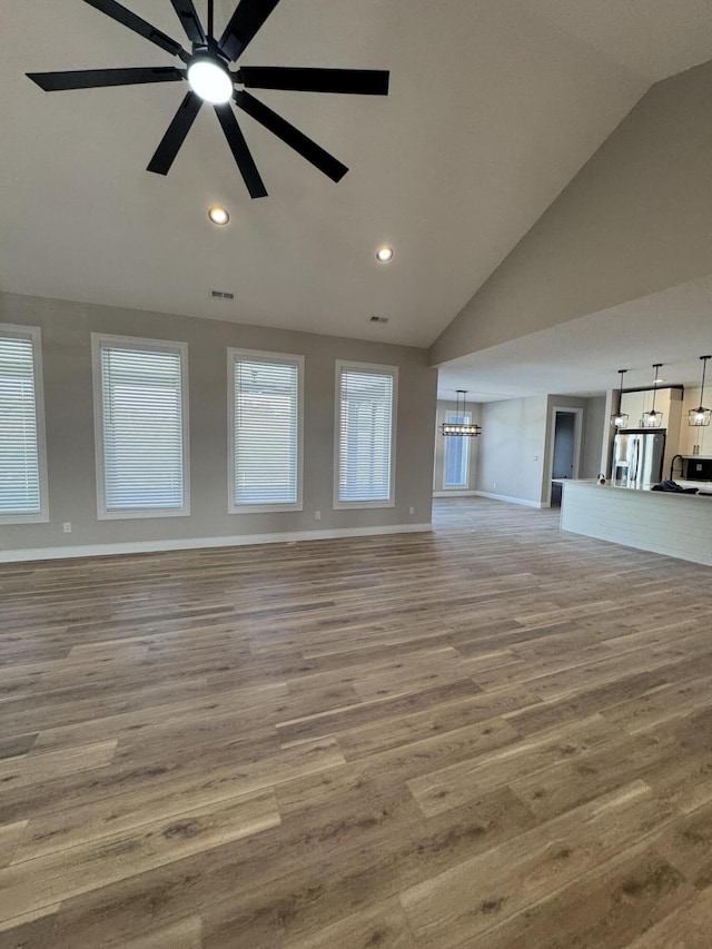 unfurnished living room featuring ceiling fan with notable chandelier, lofted ceiling, and light hardwood / wood-style floors