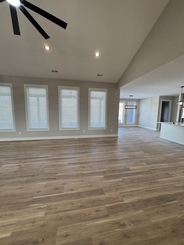 unfurnished living room with hardwood / wood-style flooring, vaulted ceiling, and ceiling fan with notable chandelier