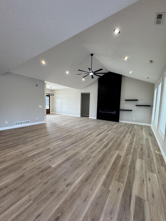 unfurnished living room featuring lofted ceiling, light hardwood / wood-style floors, and ceiling fan with notable chandelier