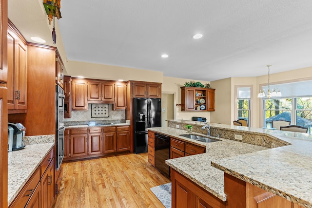 kitchen featuring light hardwood / wood-style flooring, hanging light fixtures, sink, black appliances, and light stone counters